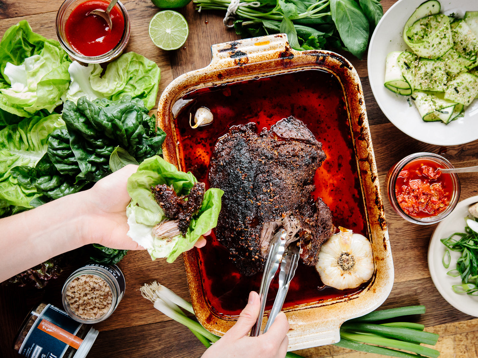 Cooked pork shoulder being served into lettuce, with surrounding ingredients