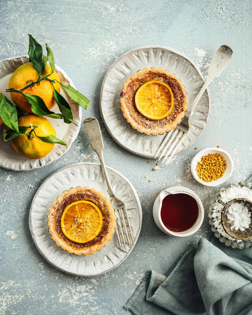 Plates with citrus tarts, a plate of citrus, a jar of honey, and a bowl of salt.