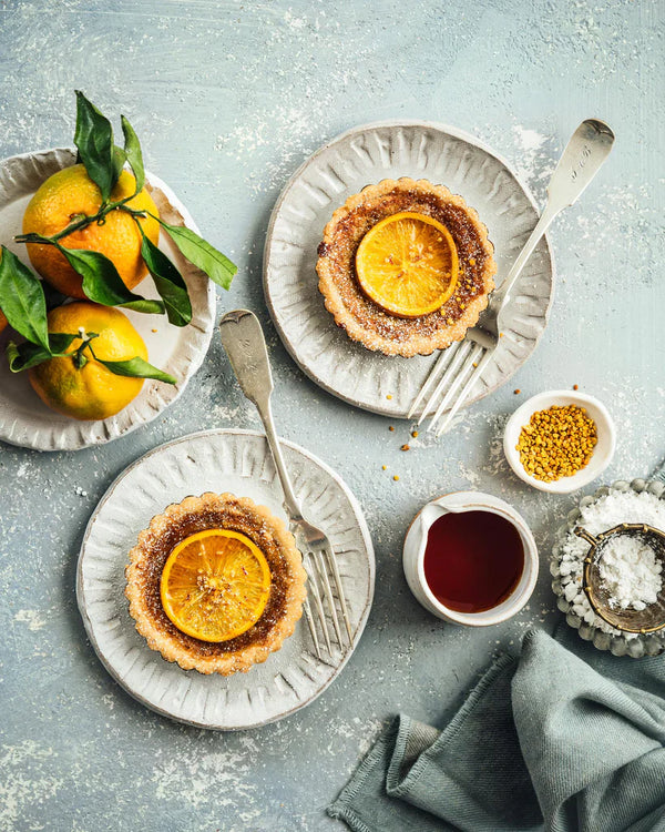 Plates with citrus tarts, a plate of citrus, a jar of honey, and a bowl of salt.