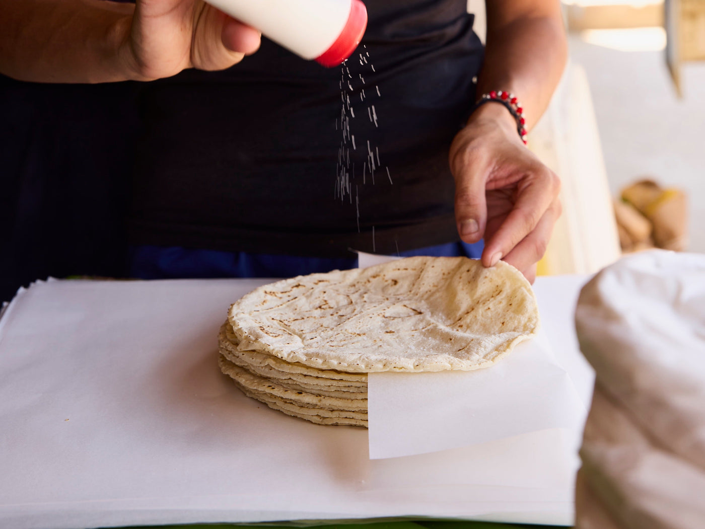 A person shakes a salt shaker over fresh tortillas.