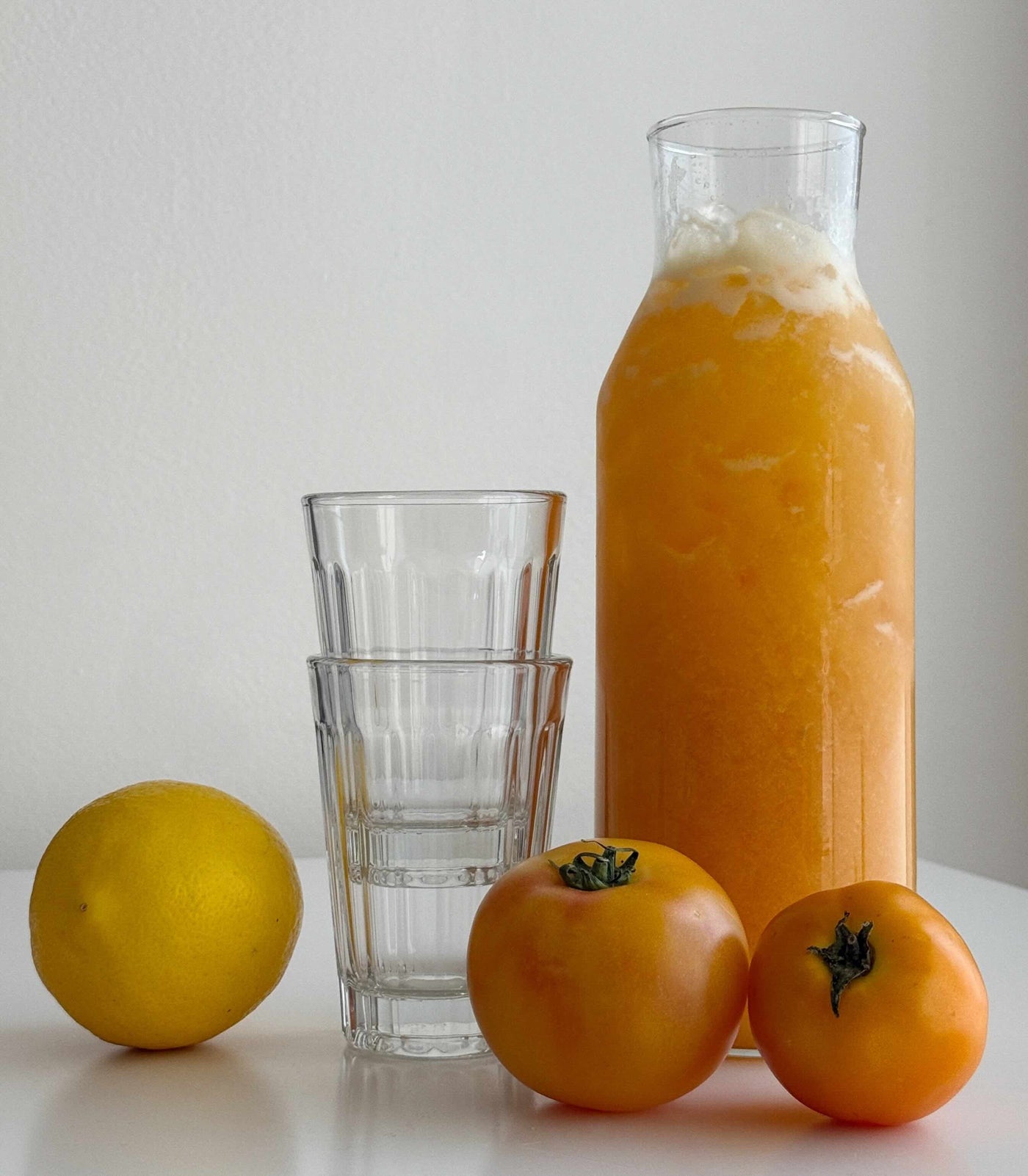 Salted Tomato Lemonade in a pitcher, with serving glasses, tomatoes and lemon.