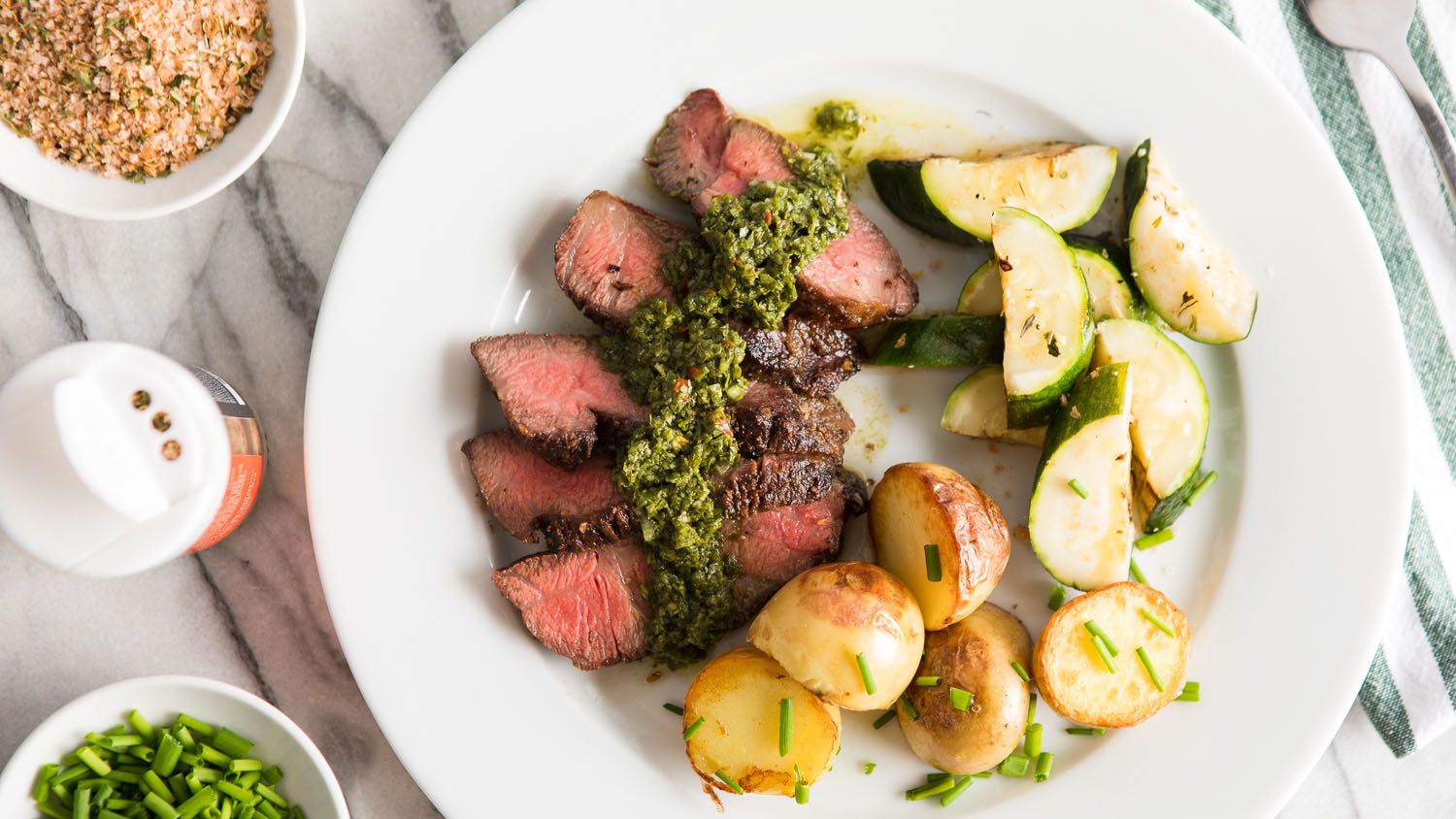 A plate with sliced grilled steak, potatoes and cooked cucumber.