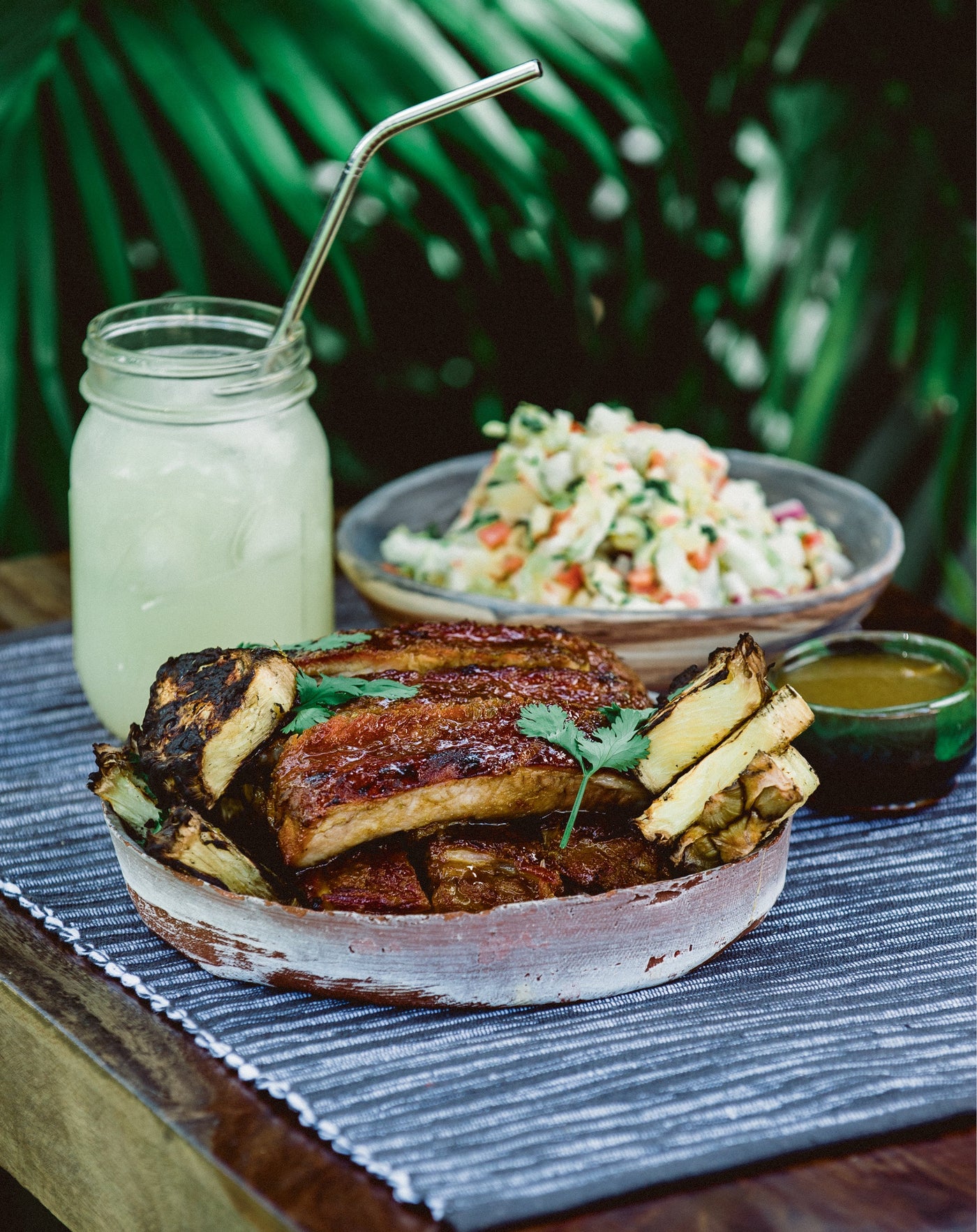 A plate of grilled ribs next to a bowl of vegetables and a glass of lemonade.