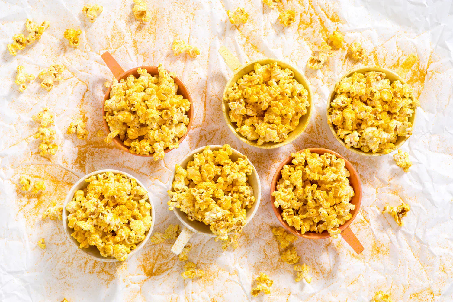 Six small bowls of golden popcorn.