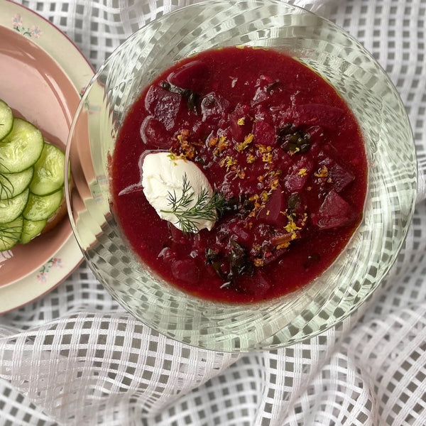 A clear glass bowl filled with red soup, garnished with labneh and a sprig of dill.
