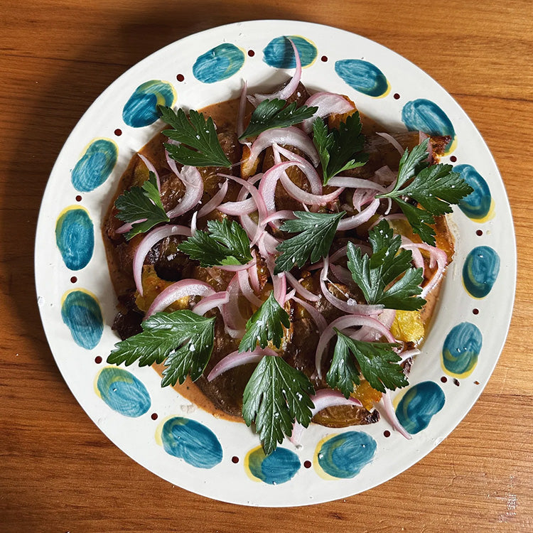 A plate of crispy potatoes, covered in sauce, onions and parsley.