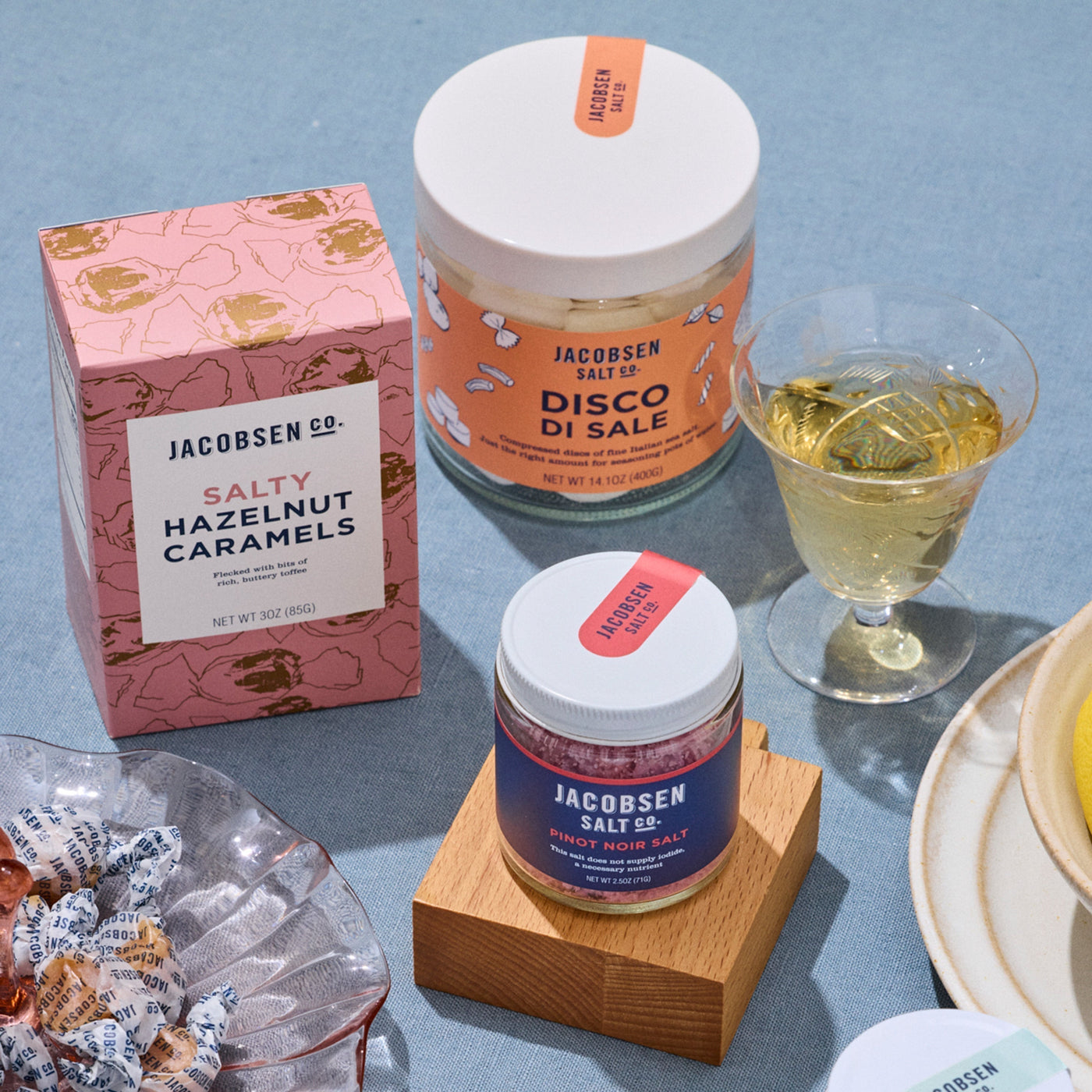 A box of Salty Hazelnut Caramels, Disco di Sale and Pinot Noir Salt on a blue tabletop.