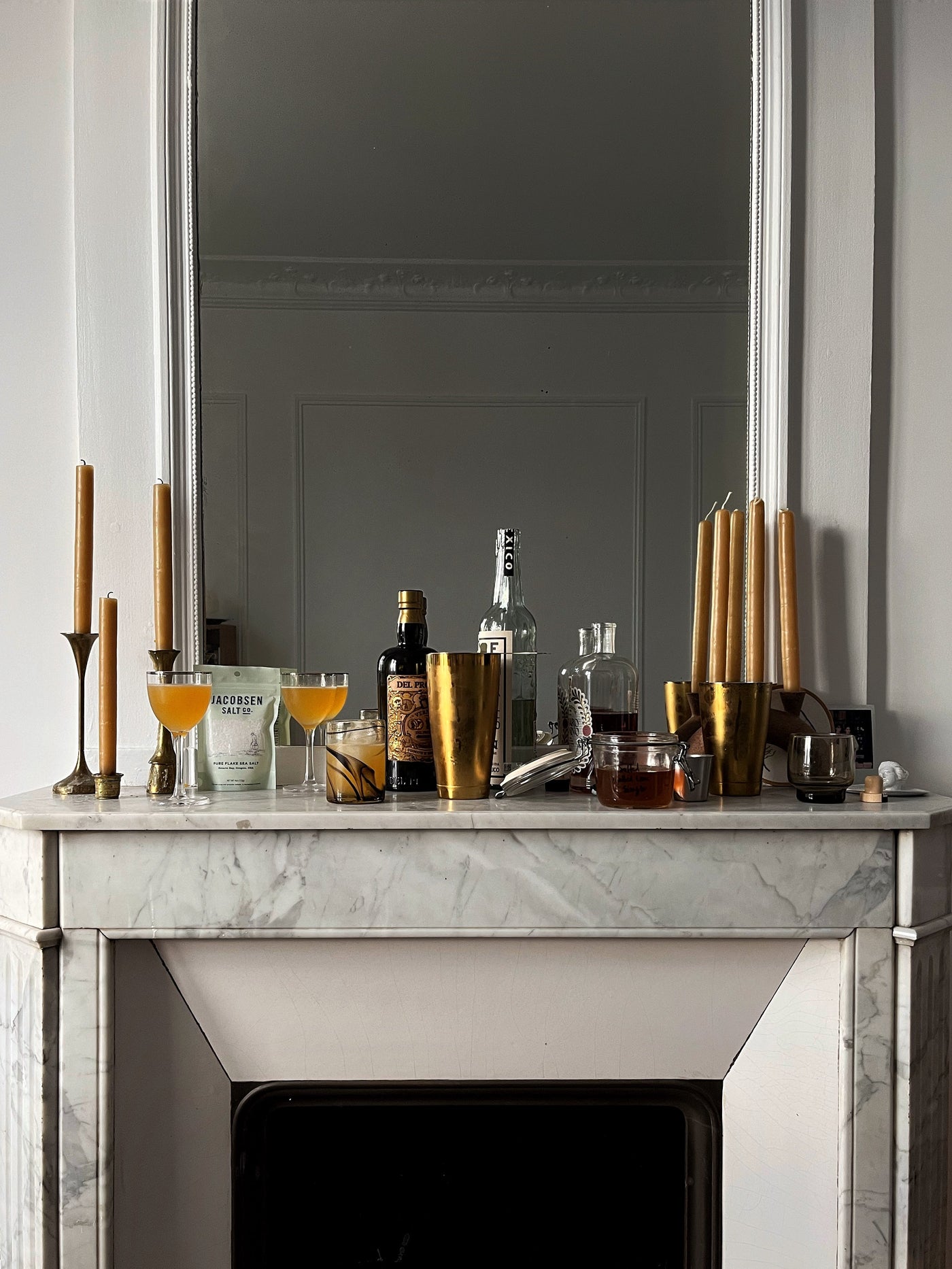 Equipment to make cocktails, along with decorative candles, sits atop a fireplace mantel.