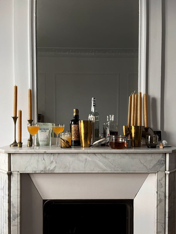 Equipment to make cocktails, along with decorative candles, sits atop a fireplace mantel.