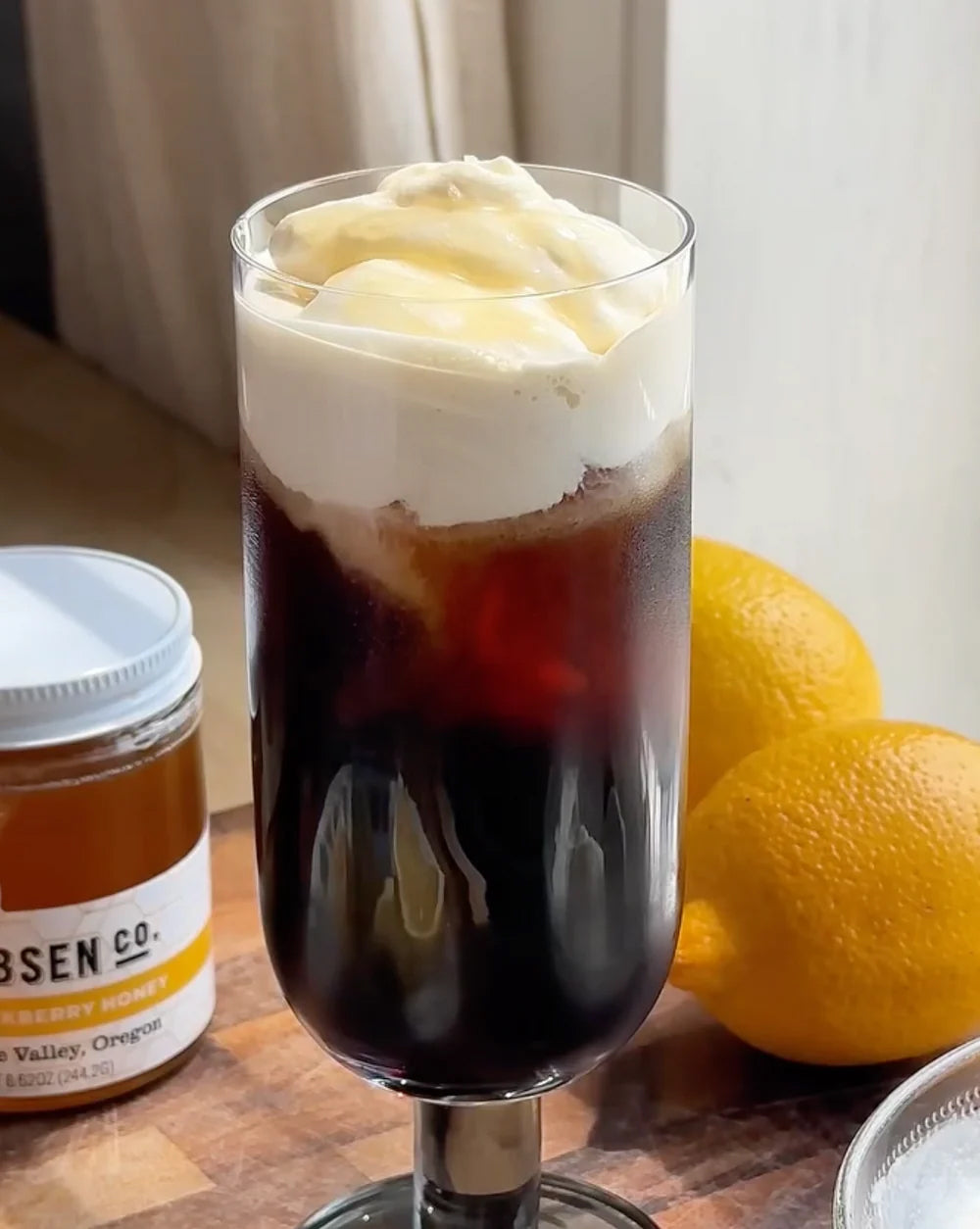 Tall glass of coldbrew, a dark brown beverage topped with white foam.