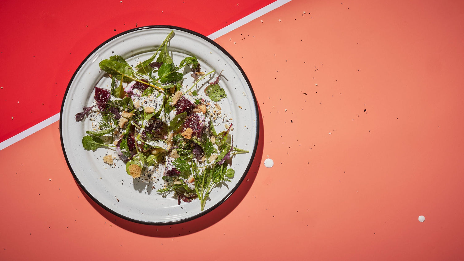 A beet salad on a circular white plate on a red and orange background.
