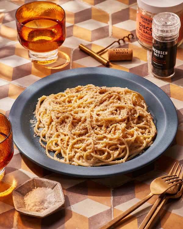 Pasta topped with pecorino romano cheese on a blue plate, on top of a geometric patterned tabletop.