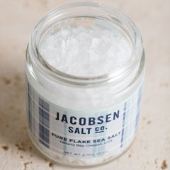 An open jar of Jacobsen Pure Flake Sea Salt with visible salt crystals. 