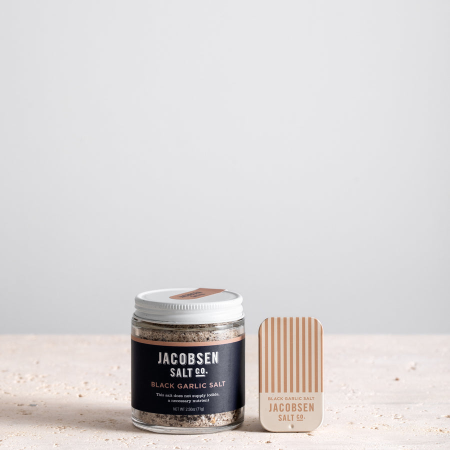 A jar of Jacobsen Infused Black Garlic Salt next to a matching slide tin of the same product. 
