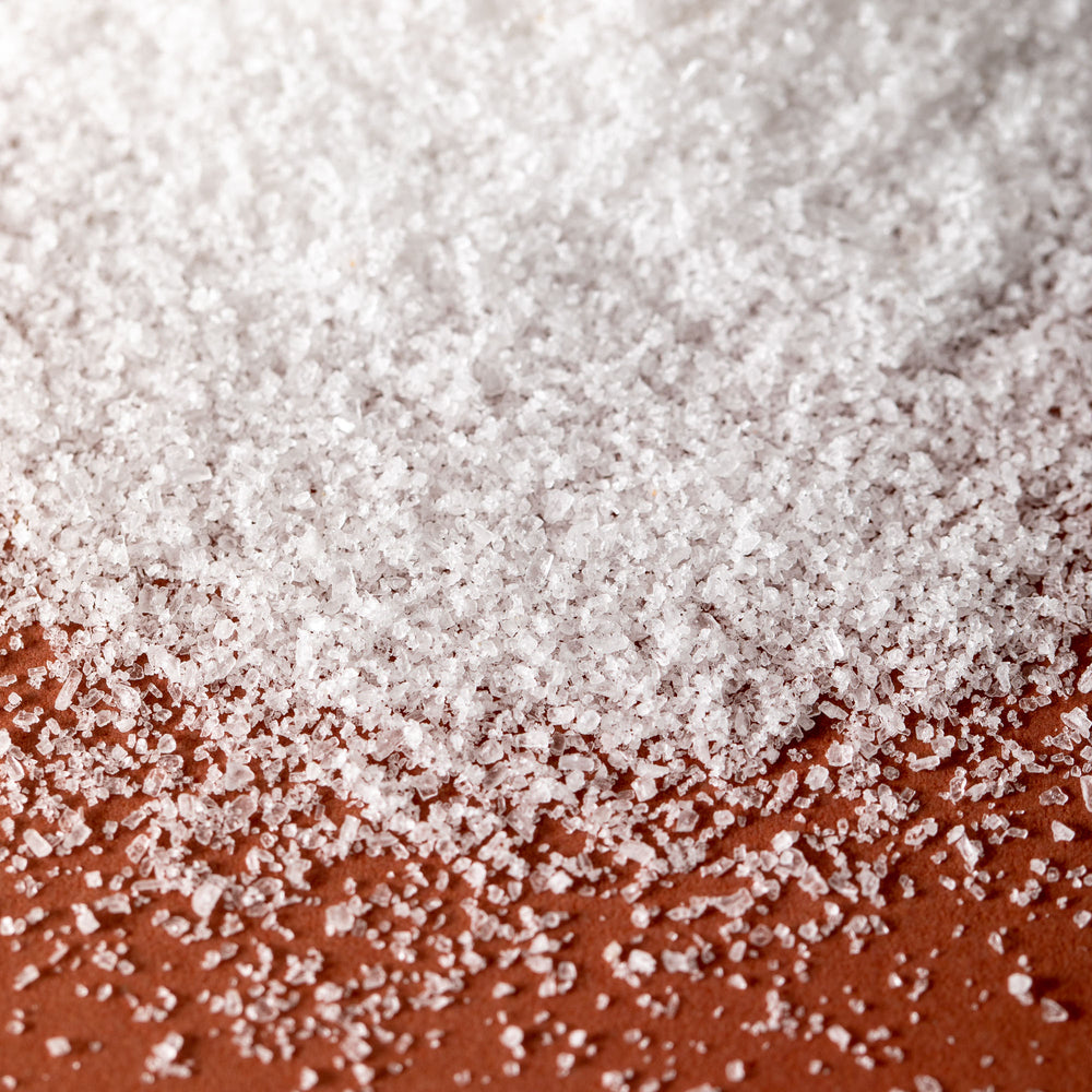 Detail of Jacobsen Pure Fine Italian Salt, on an orange tabletop. 