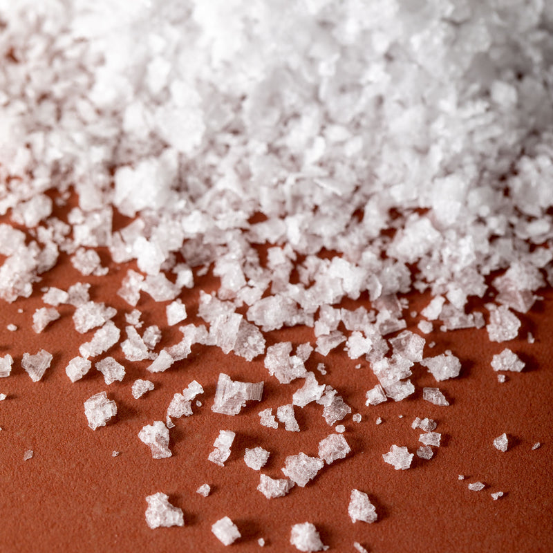 Detail of Jacobsen Pure Flake Sea Salt, on an orange tabletop. 