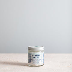 A glass jar of Jacobsen Pure Flake Sea Salt on a neutral background.