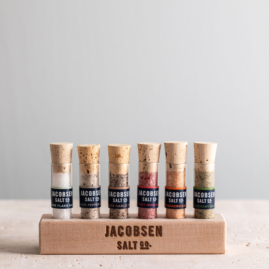 Six vials of Jacobsen pure and infused sea salts, including Flake, Black Pepper, Black Garlic, Pinot Noir, Habanero and Rosemary in a wooden branded stand