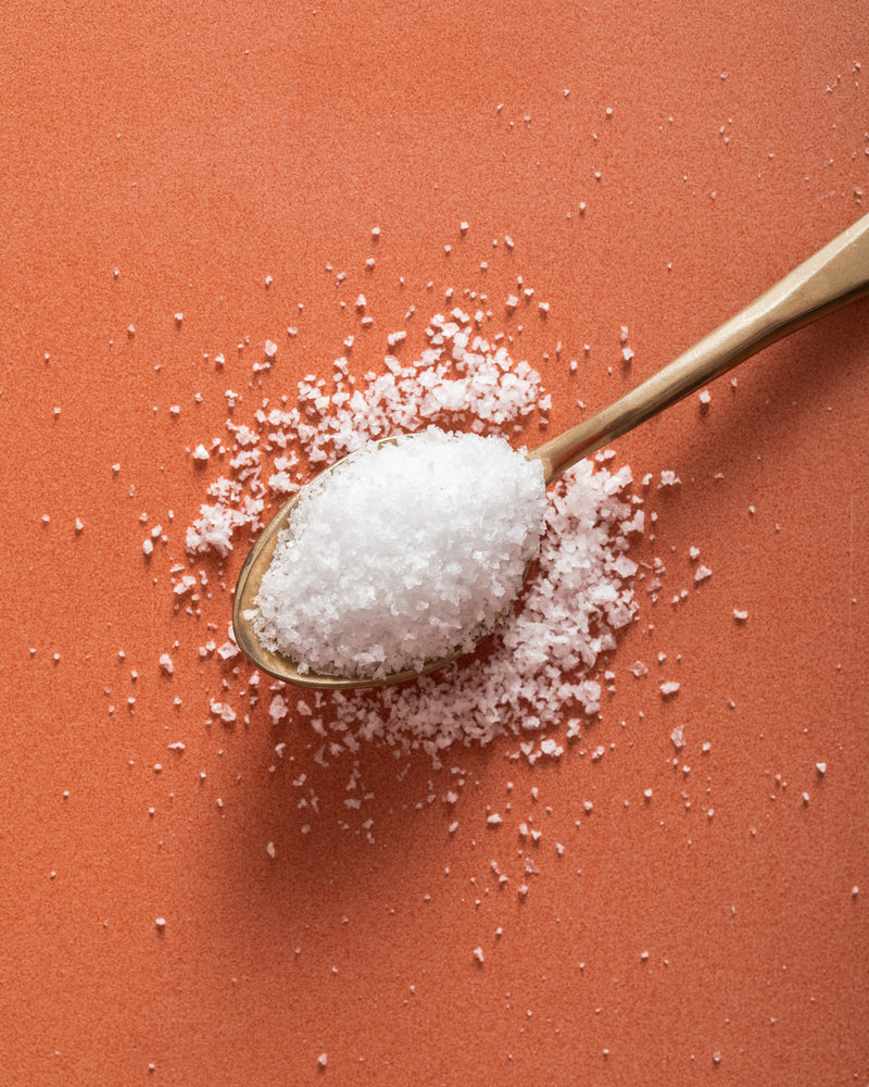 A spoon full of Jacobsen Kosher Sea Salt, laying on an orange tabletop. 