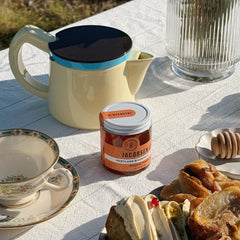 A jar of Portland Riverfont Honey at a sunny picnic with a teacup, tea kettle and pastries